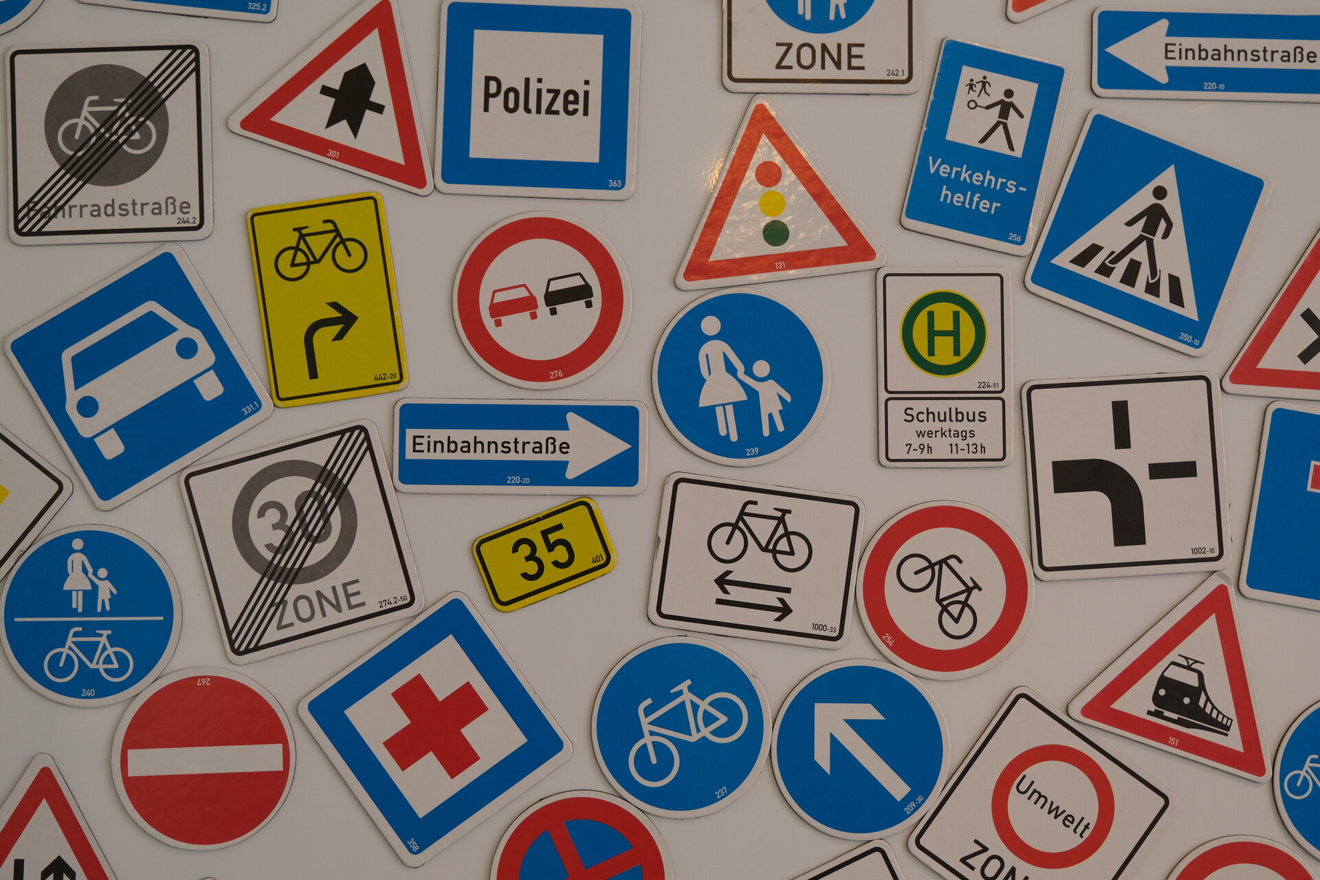 Nahaufnahme einer Sammlung verschiedener deutscher Verkehrszeichen (z.B. Einbahnstraße, Zone 30 Ende, Haltestelle, Überholverbot, Fahrradstraße), die dicht beieinander als Lehrmaterial angeordnet sind.